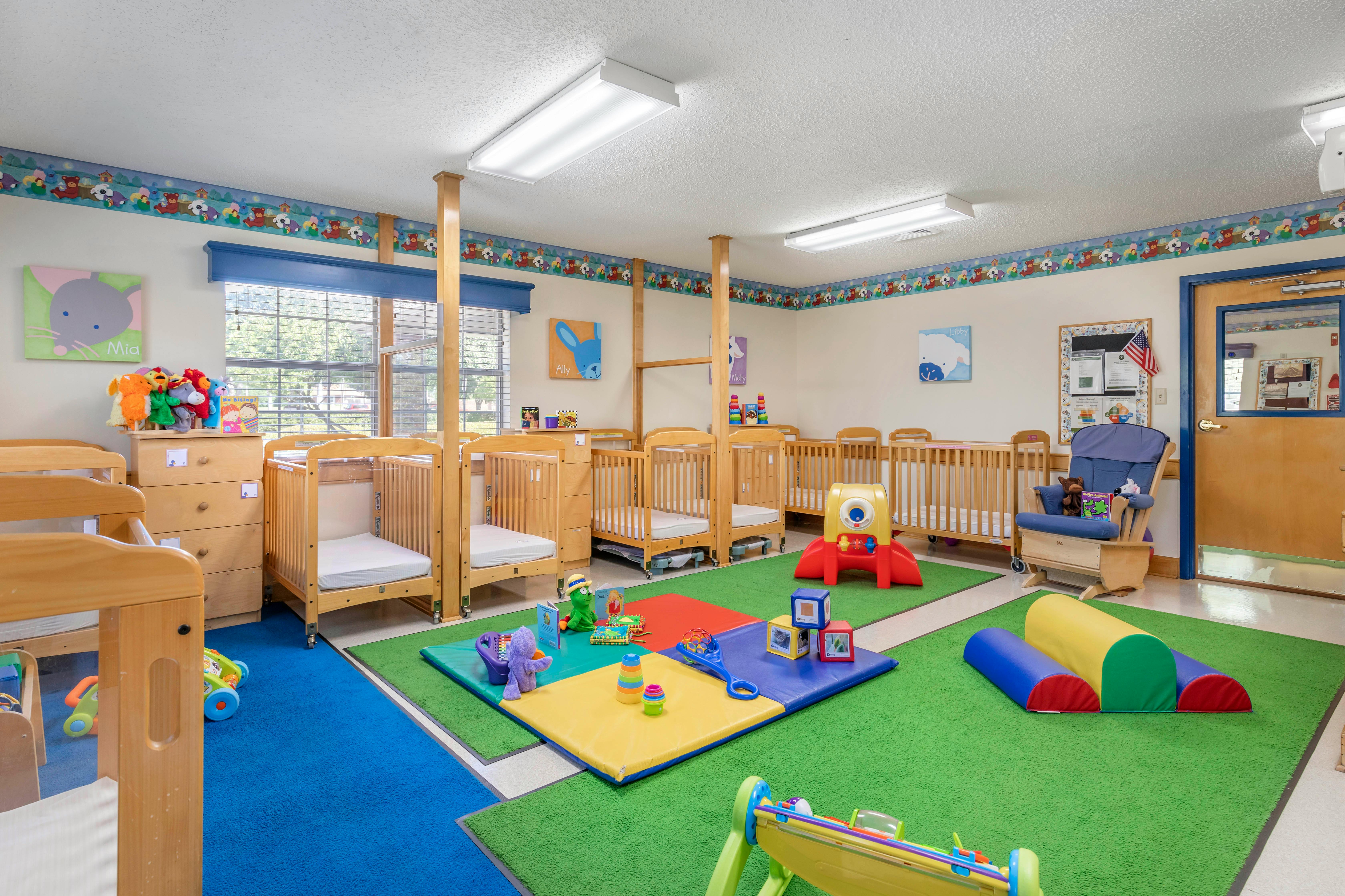 Cribs and colorful playmats with toys in a brightly lit daycare room