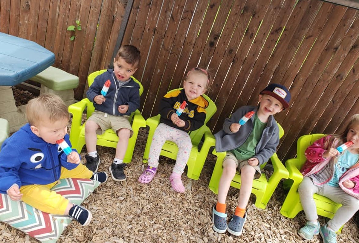 Children sitting on chairs eating popsicles outdoors