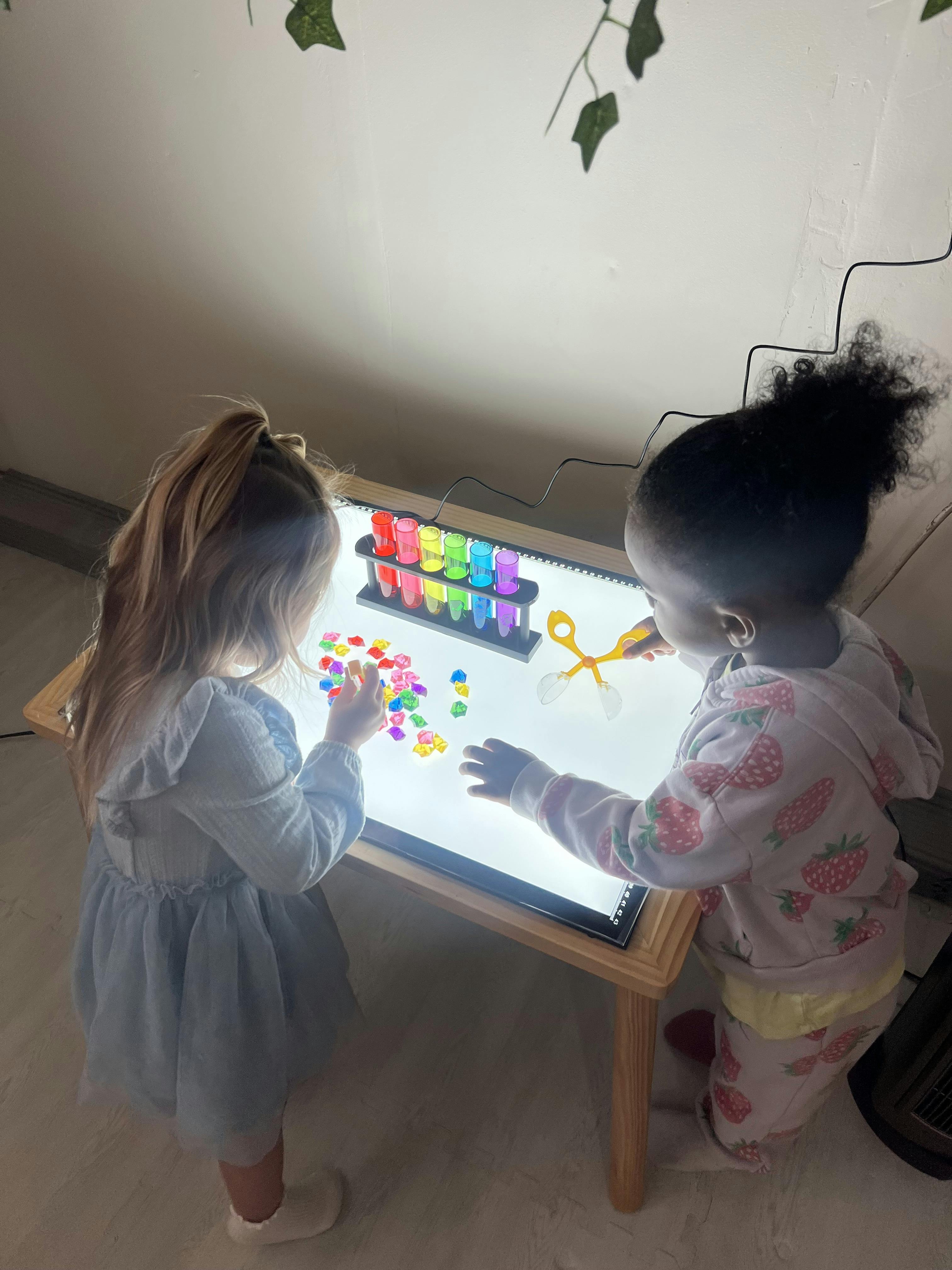 Two children playing at a light table with colorful test tubes and plastic gems