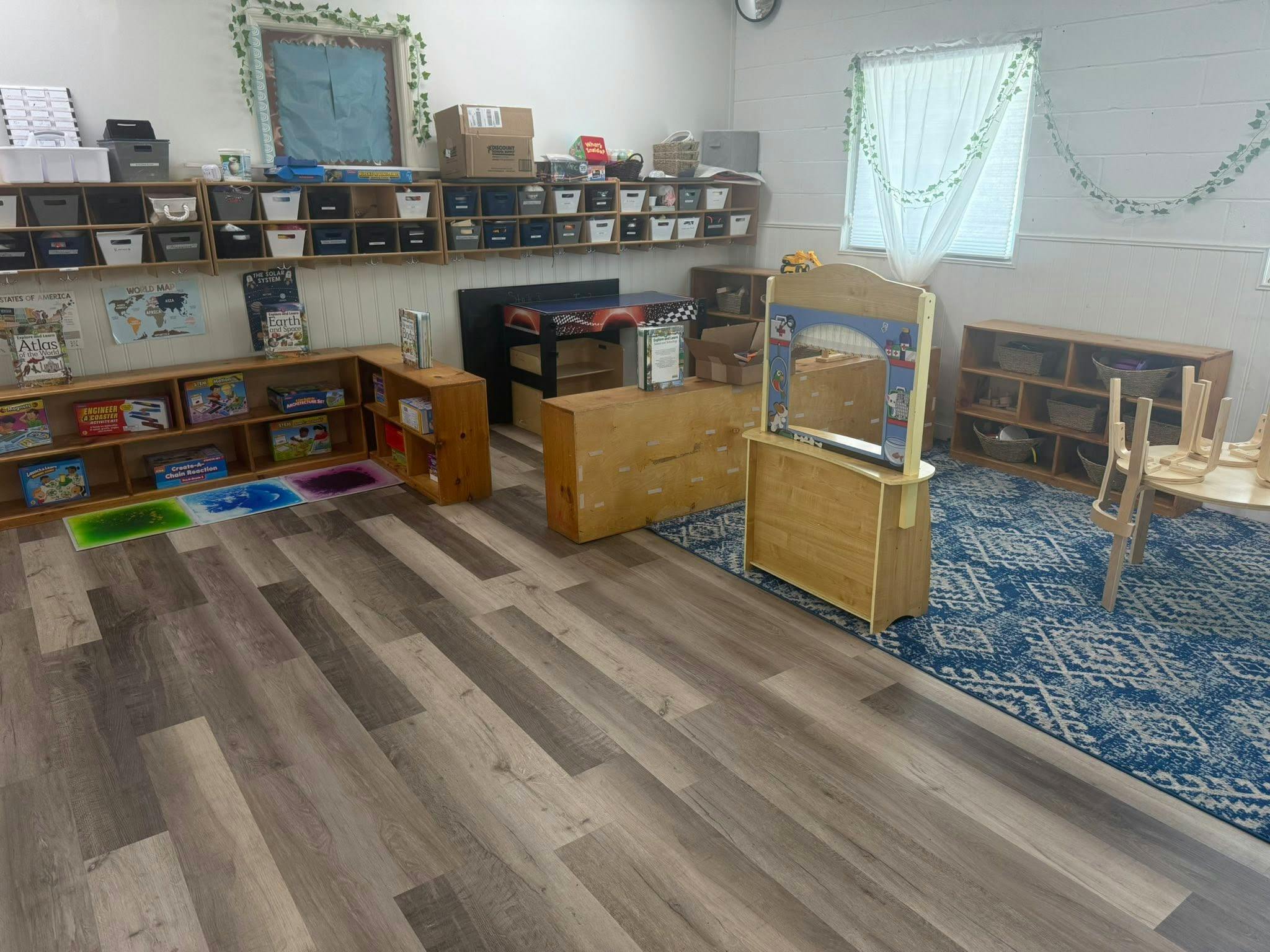 Empty classroom with wooden shelves, storage bins, and a small stage