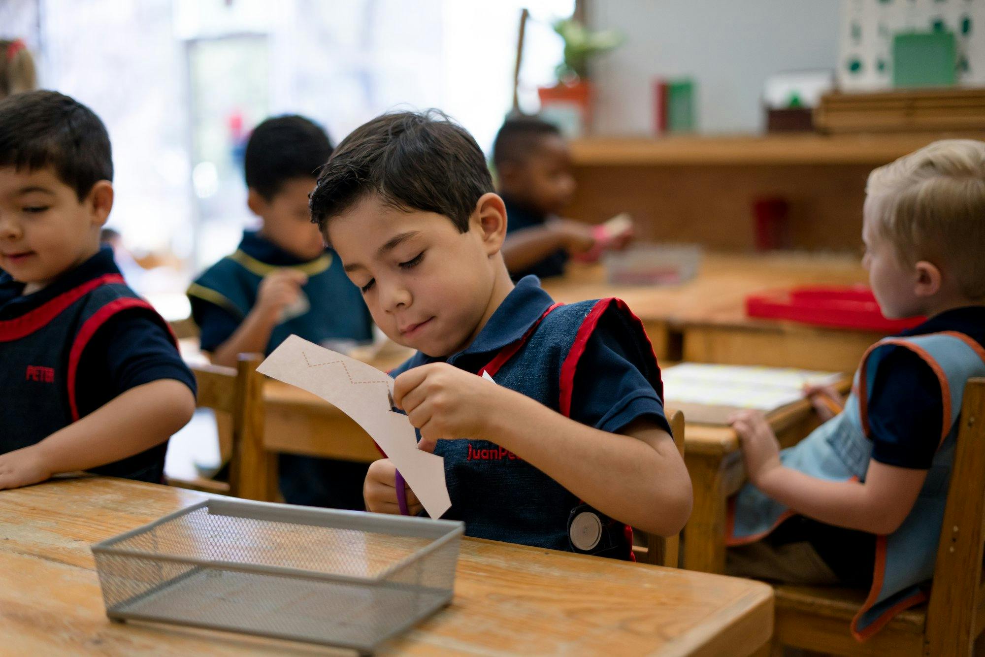 Child cutting paper at a desk in a classroom