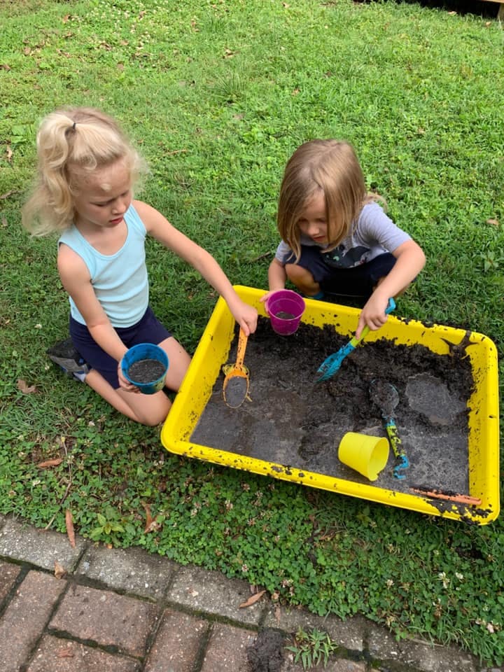 Two children playing with mud in a yellow bin outdoors container