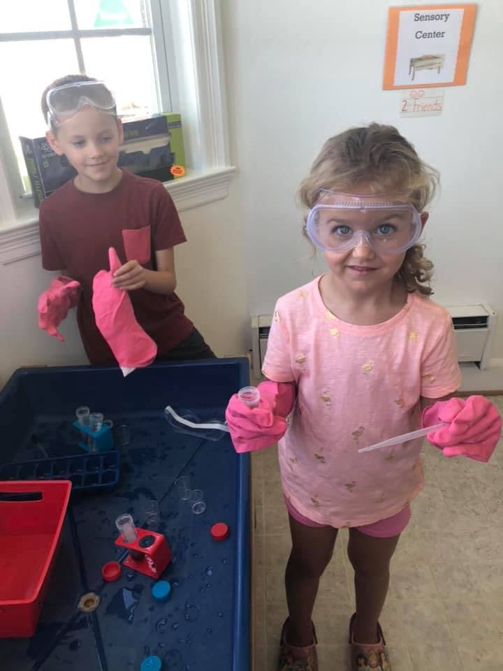 Two children wearing safety goggles and pink gloves playing with water