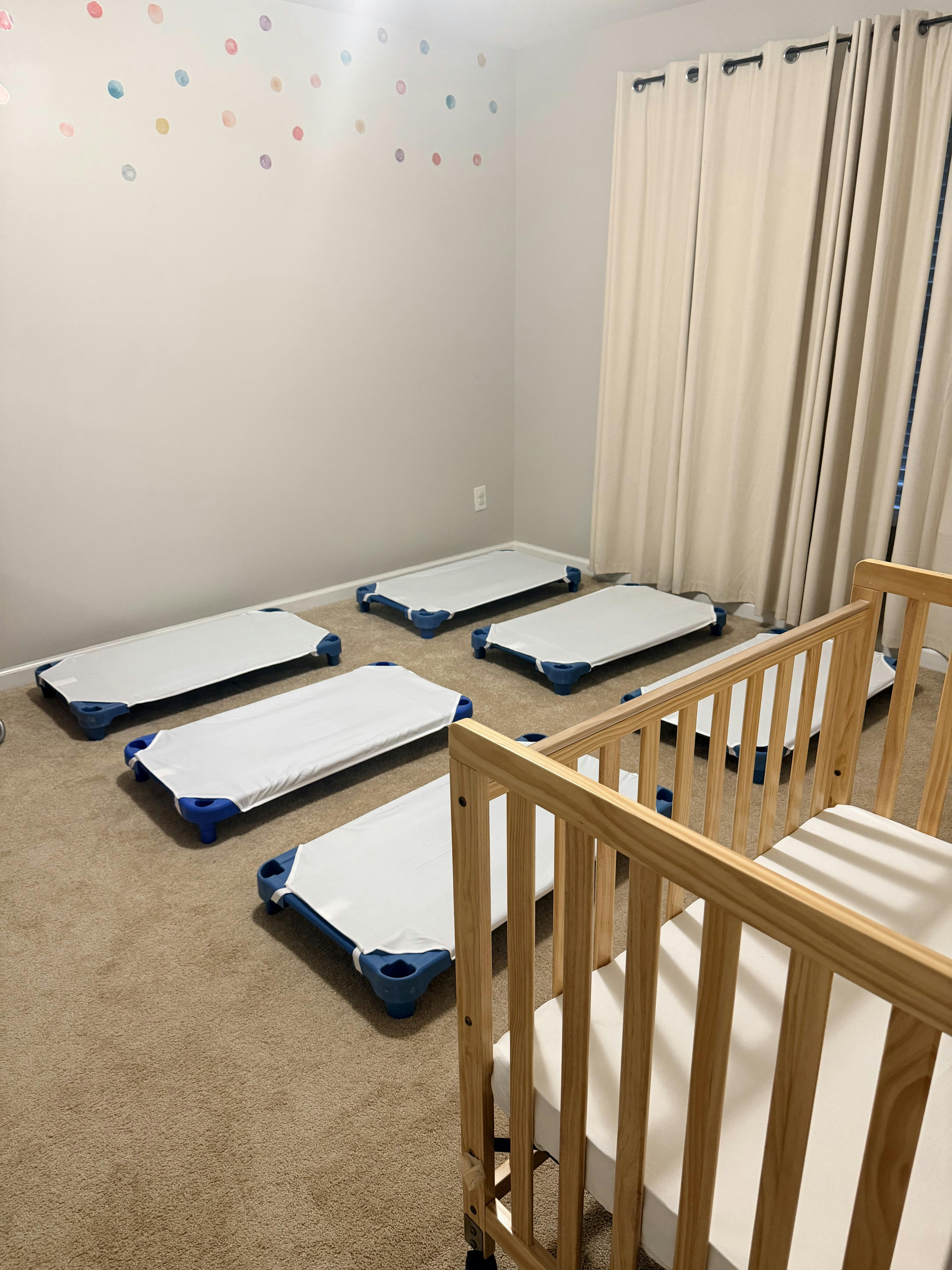 Group of child-sized sleeping cots in a room with a wooden crib
