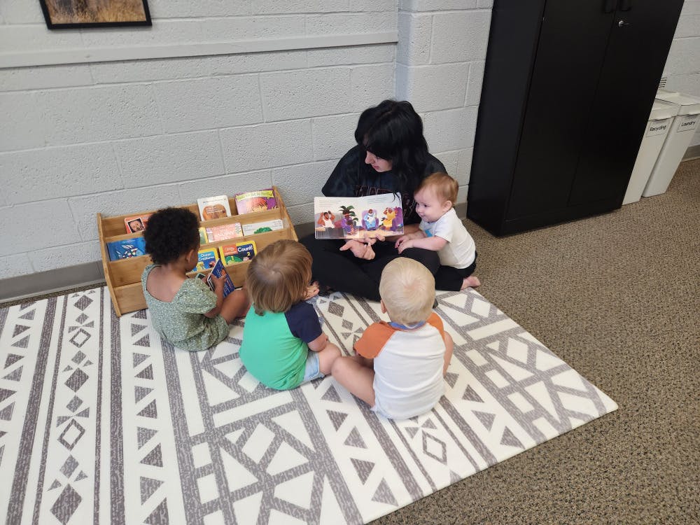 Person reading a book to three children on a rug