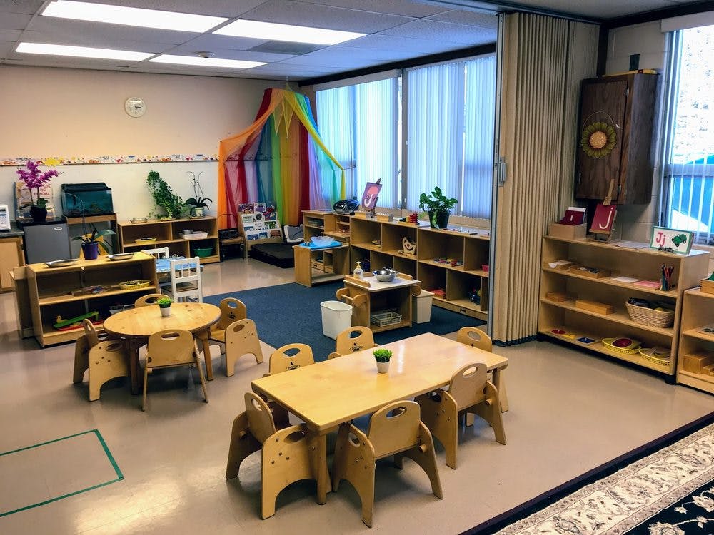 Classroom with small tables and chairs, shelves with learning materials
