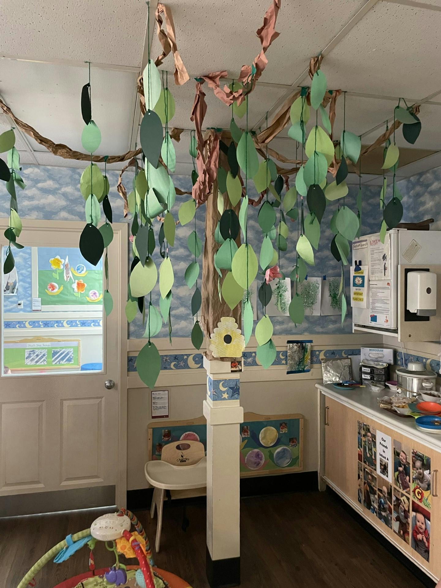 Classroom decorated with paper tree and leaves, door open to another room