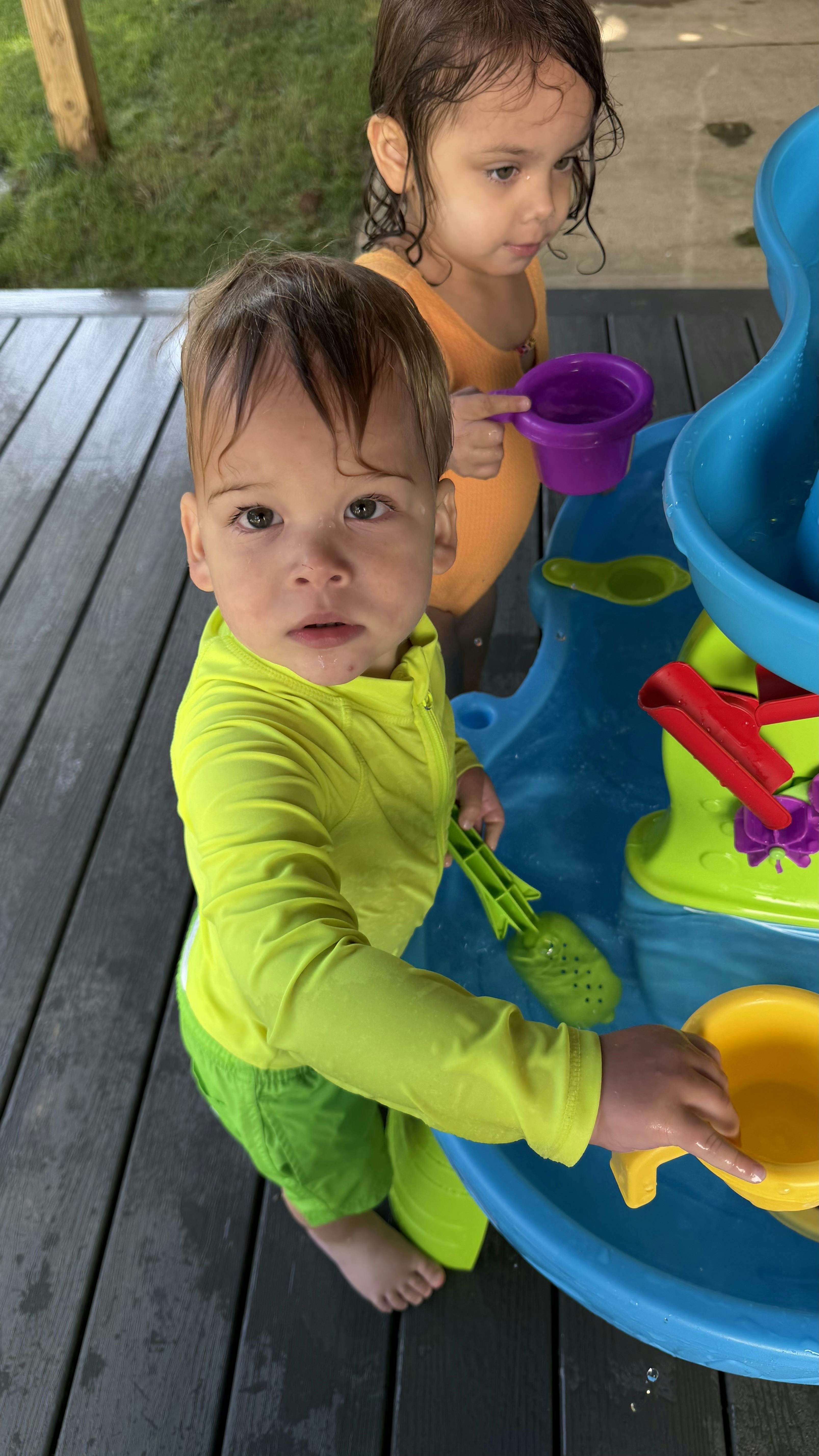 Two children playing with a water table on a wooden deck