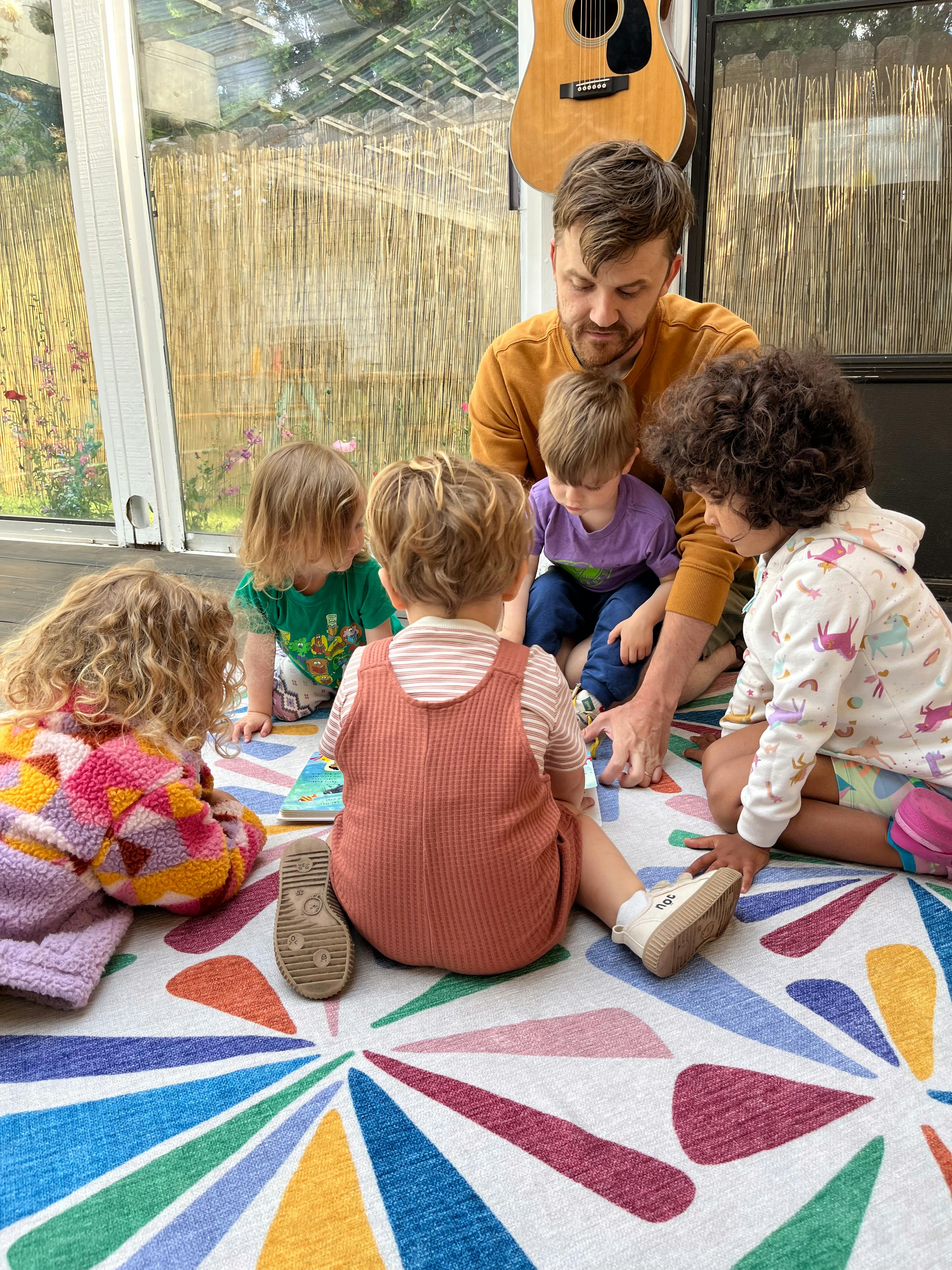 Adult and multiple children sitting on a colorful rug
