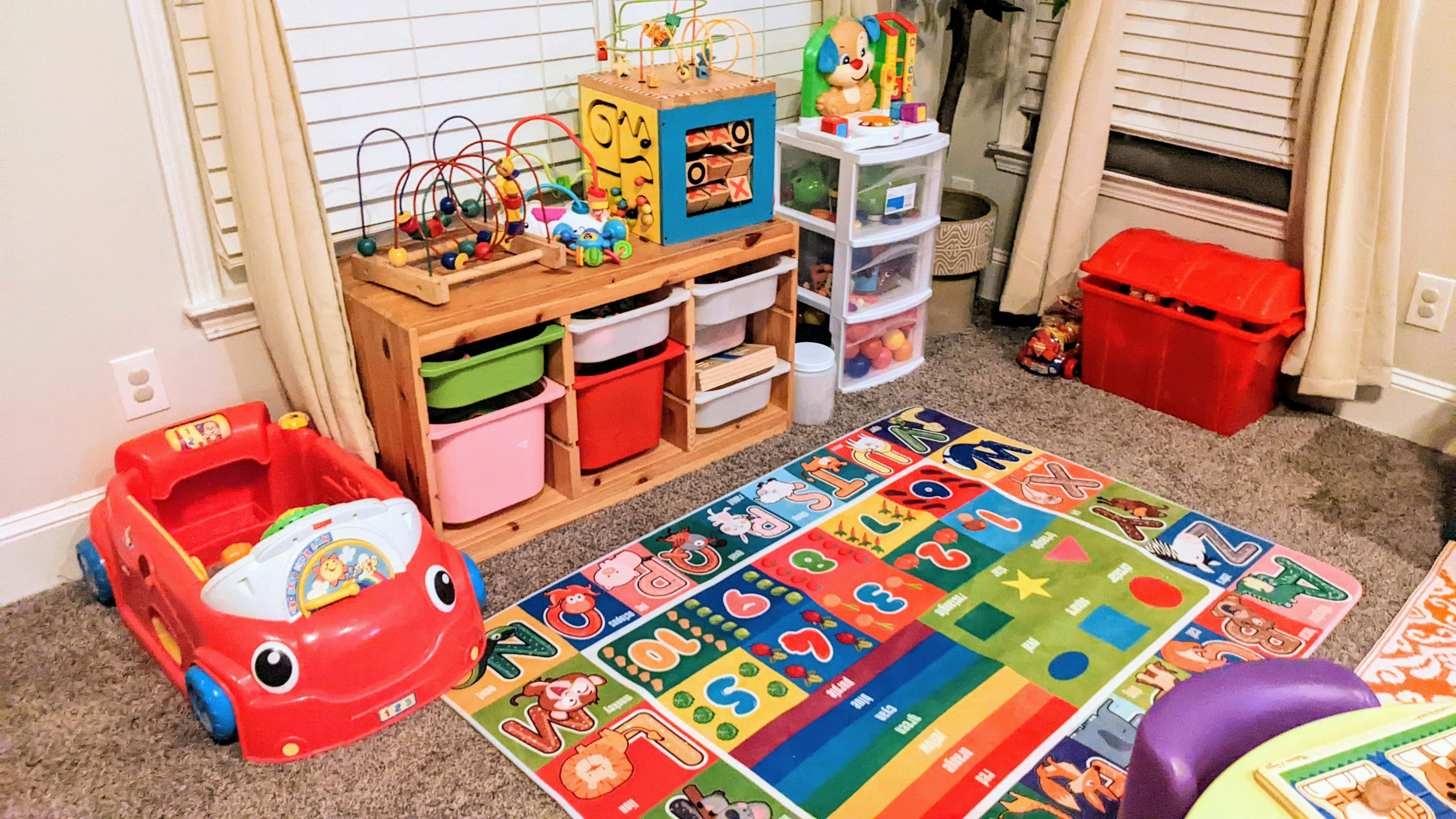 Playroom with a colorful alphabet rug, toy storage, and a red toy car