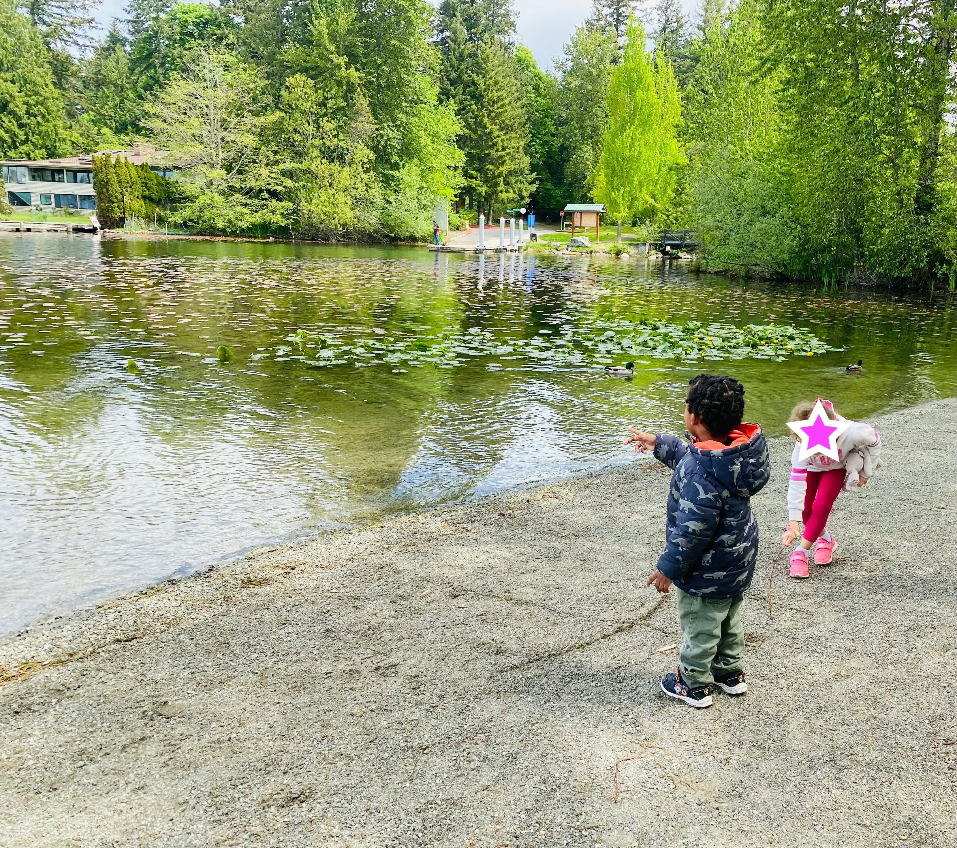 Child pointing towards a duck swimming in a lake with another child nearby