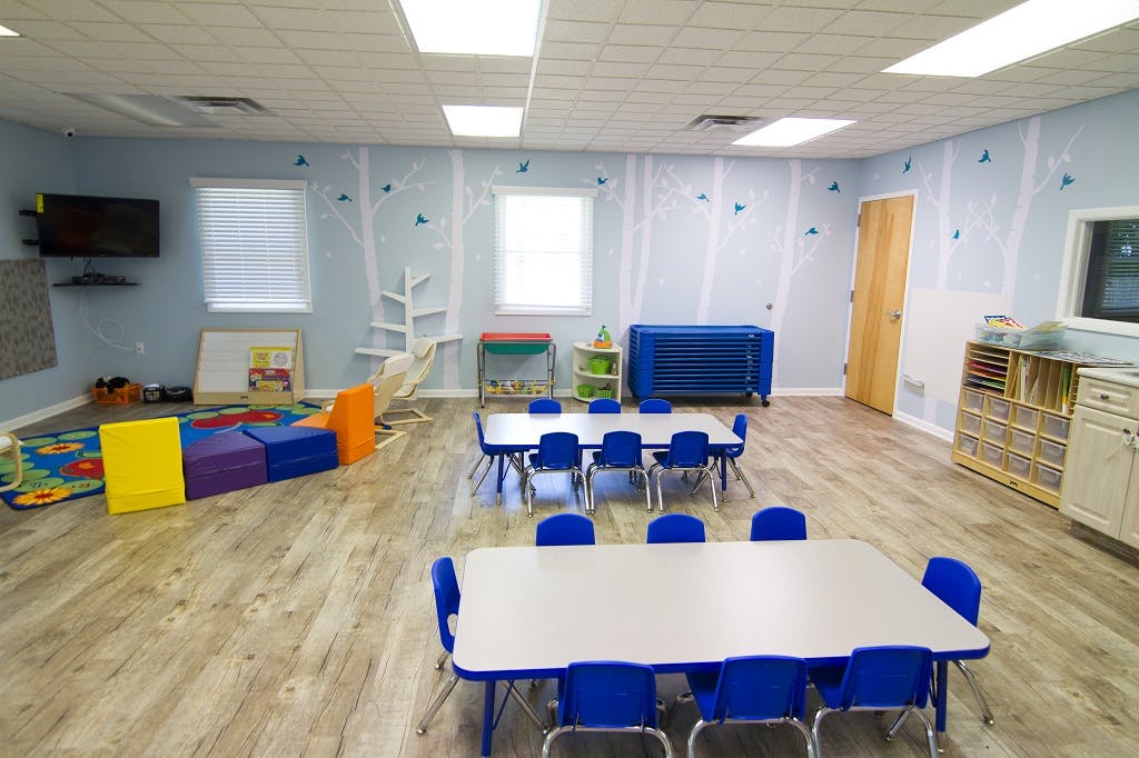 Classroom with small tables and chairs, play area with colorful blocks