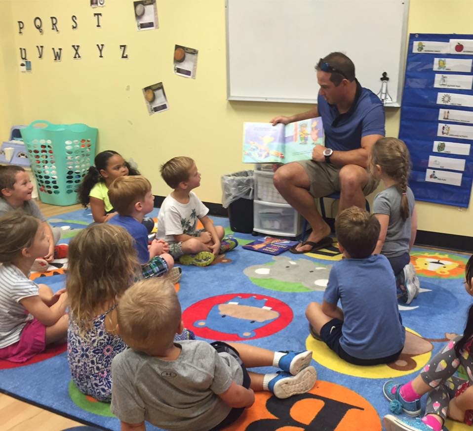 Adult reading a book to a group of children in a classroom