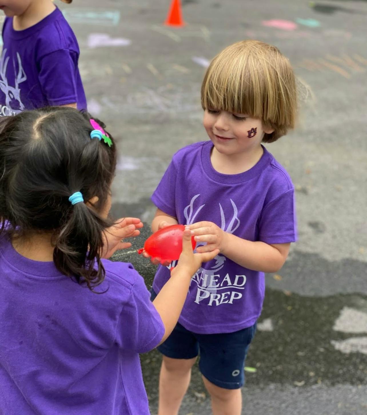 Two children playing with a red water balloon outdoors
