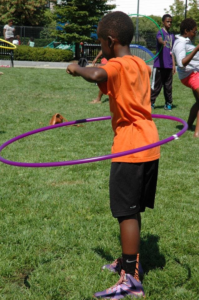 Child in orange shirt hula hooping on grass