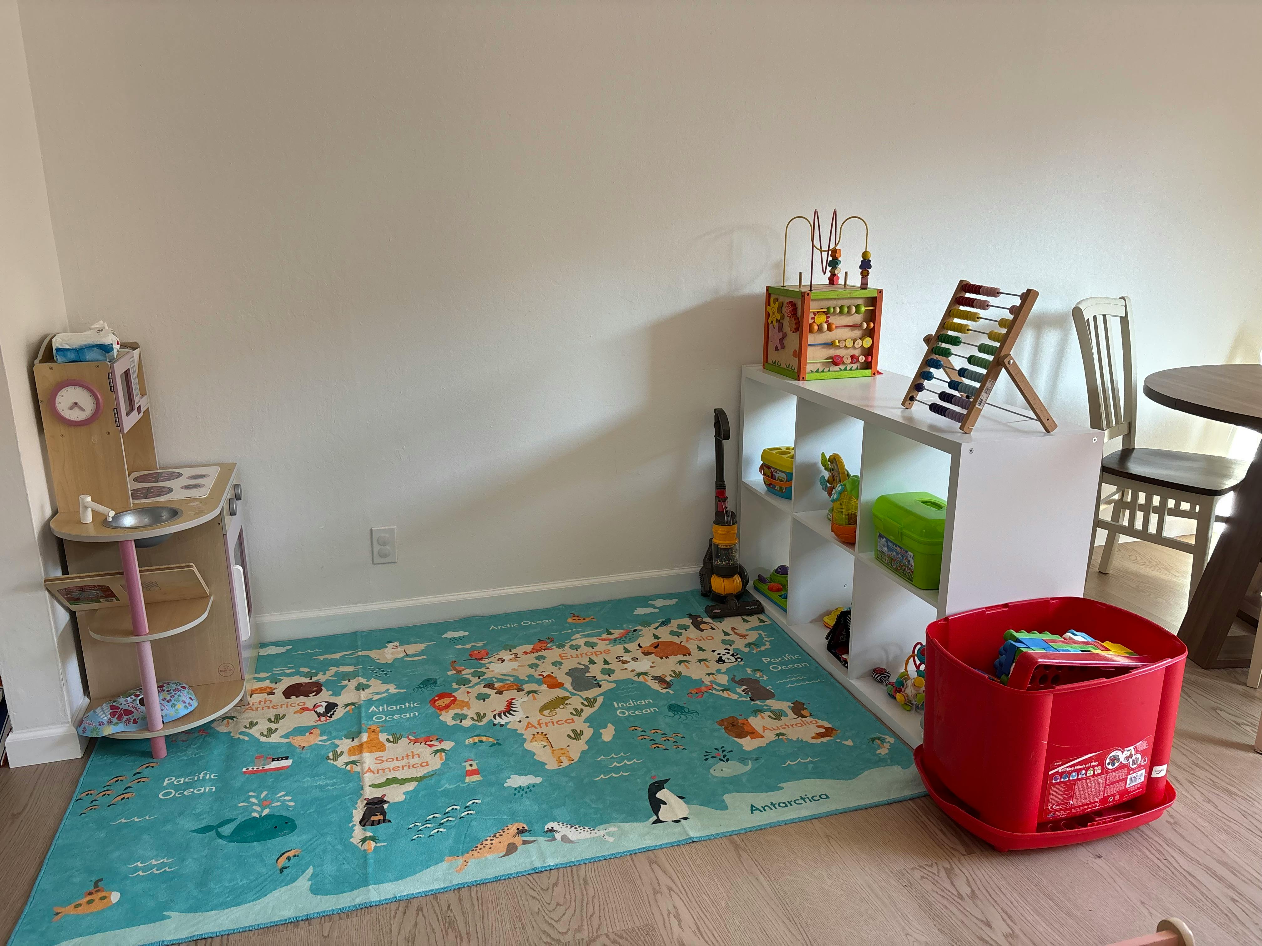 Child's playroom with a world map rug, toy kitchen, and white shelving unit with toys