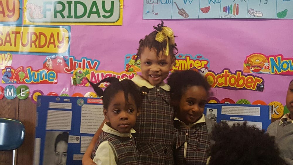 Three children in plaid uniforms standing in a classroom