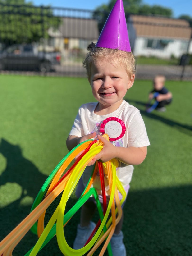 Child wearing a party hat and holding colorful plastic rings on a lawn