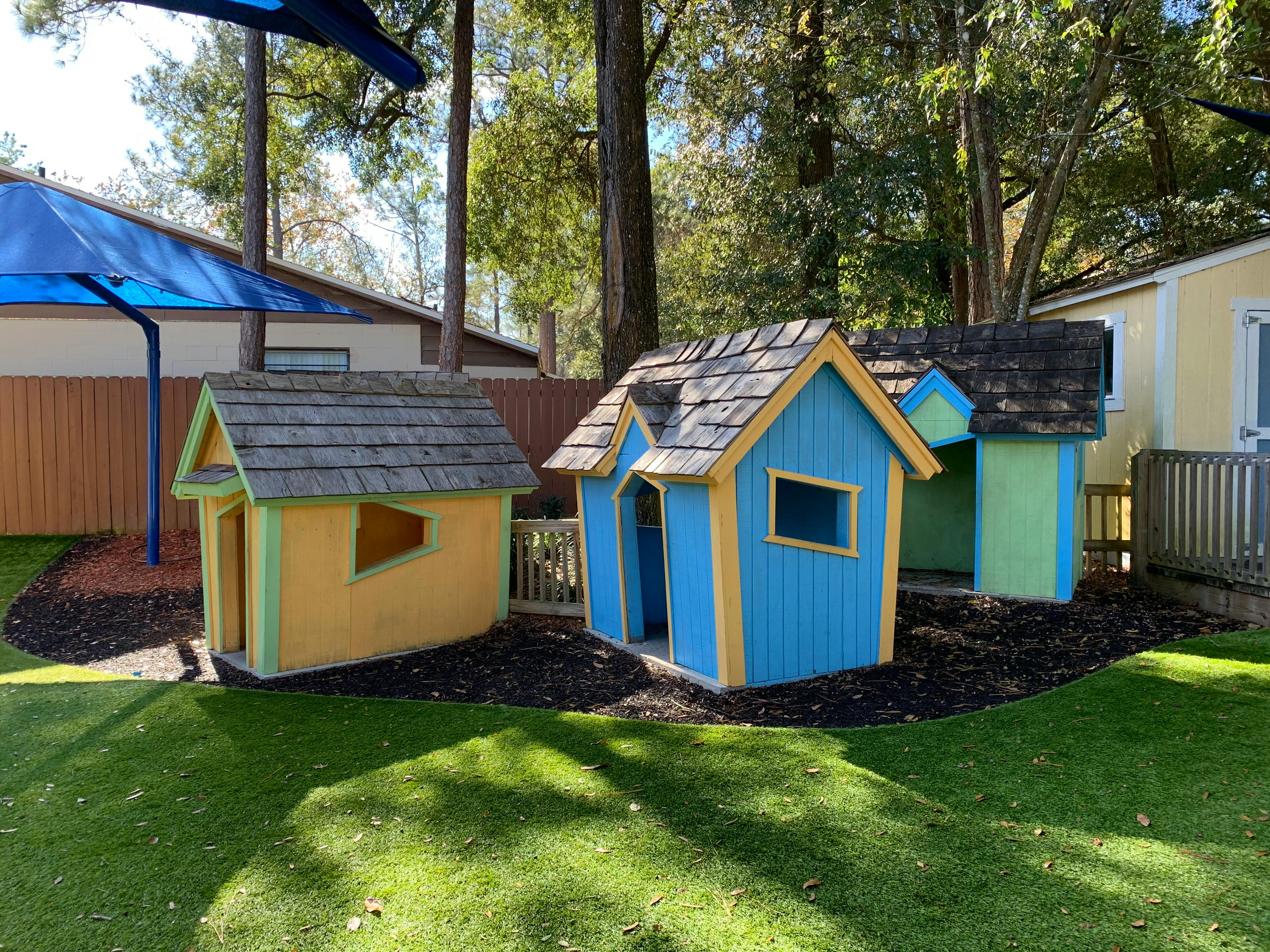 Colorful wooden playhouses on artificial turf with trees in the background