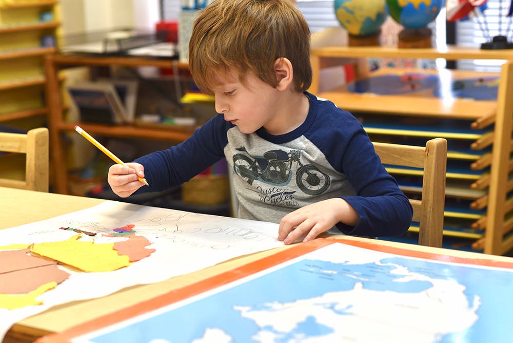 Child drawing on a large map with a pencil in a classroom