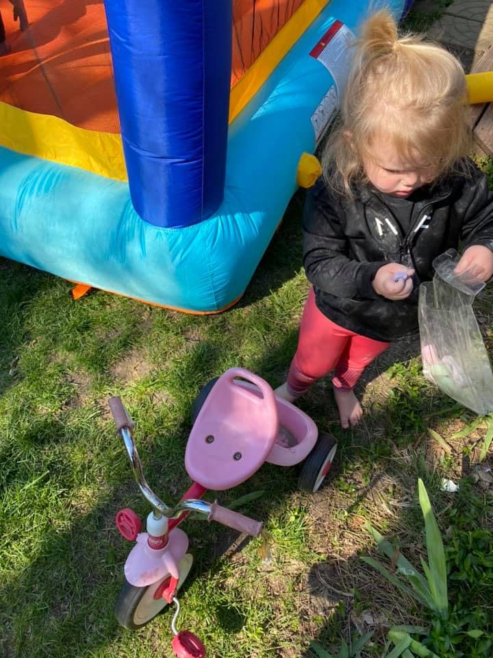Child standing next to a pink tricycle and inflatable bounce house