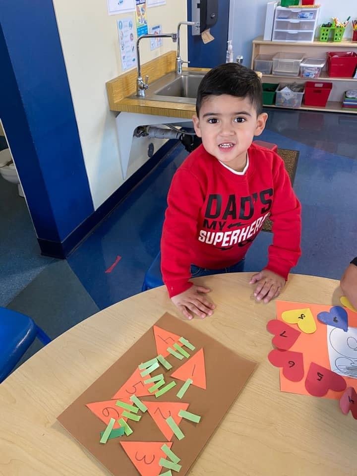 Child in a red shirt standing at a table with crafts