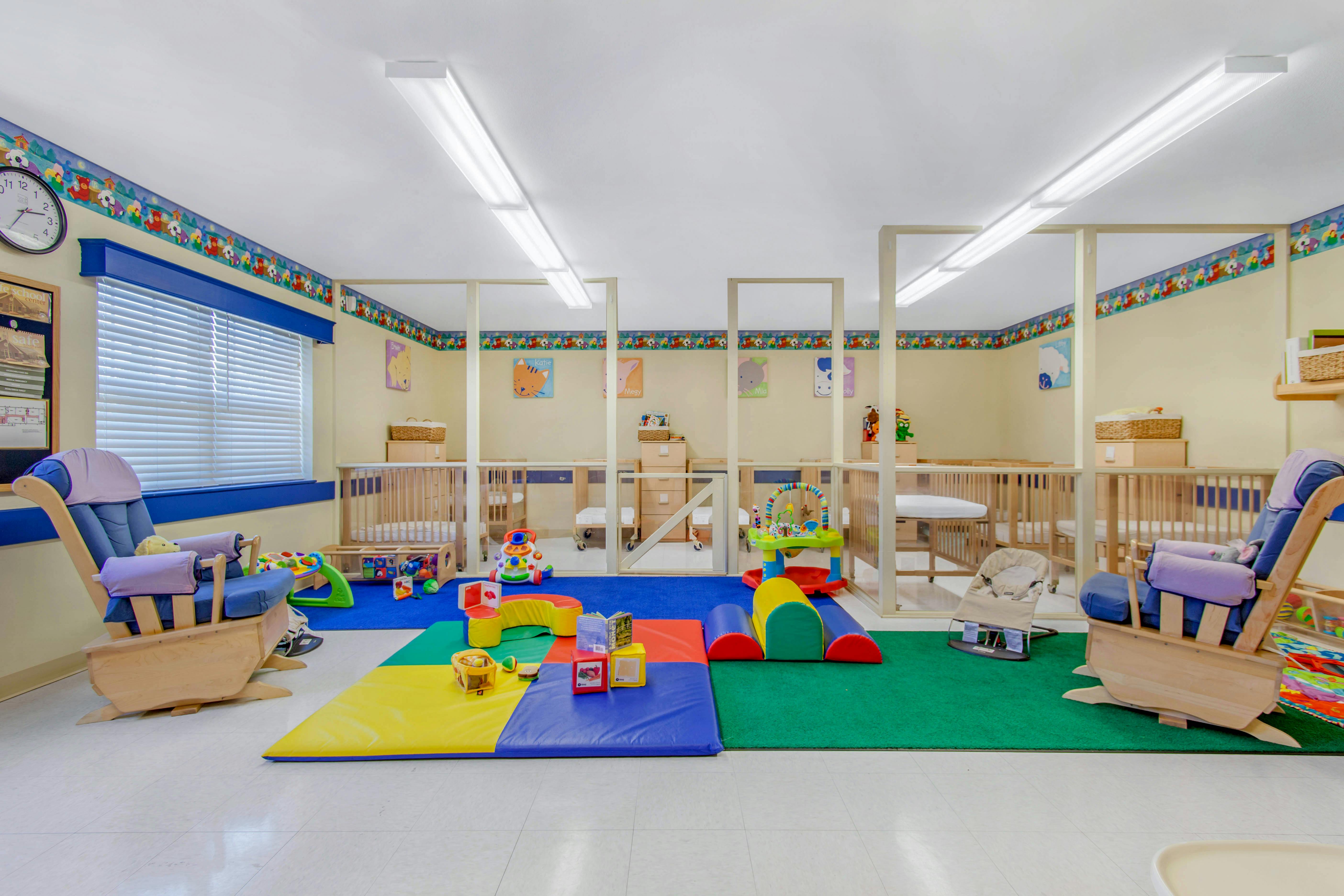 A colorful baby nursery or childcare room with cribs, playmats, and rocking chairs