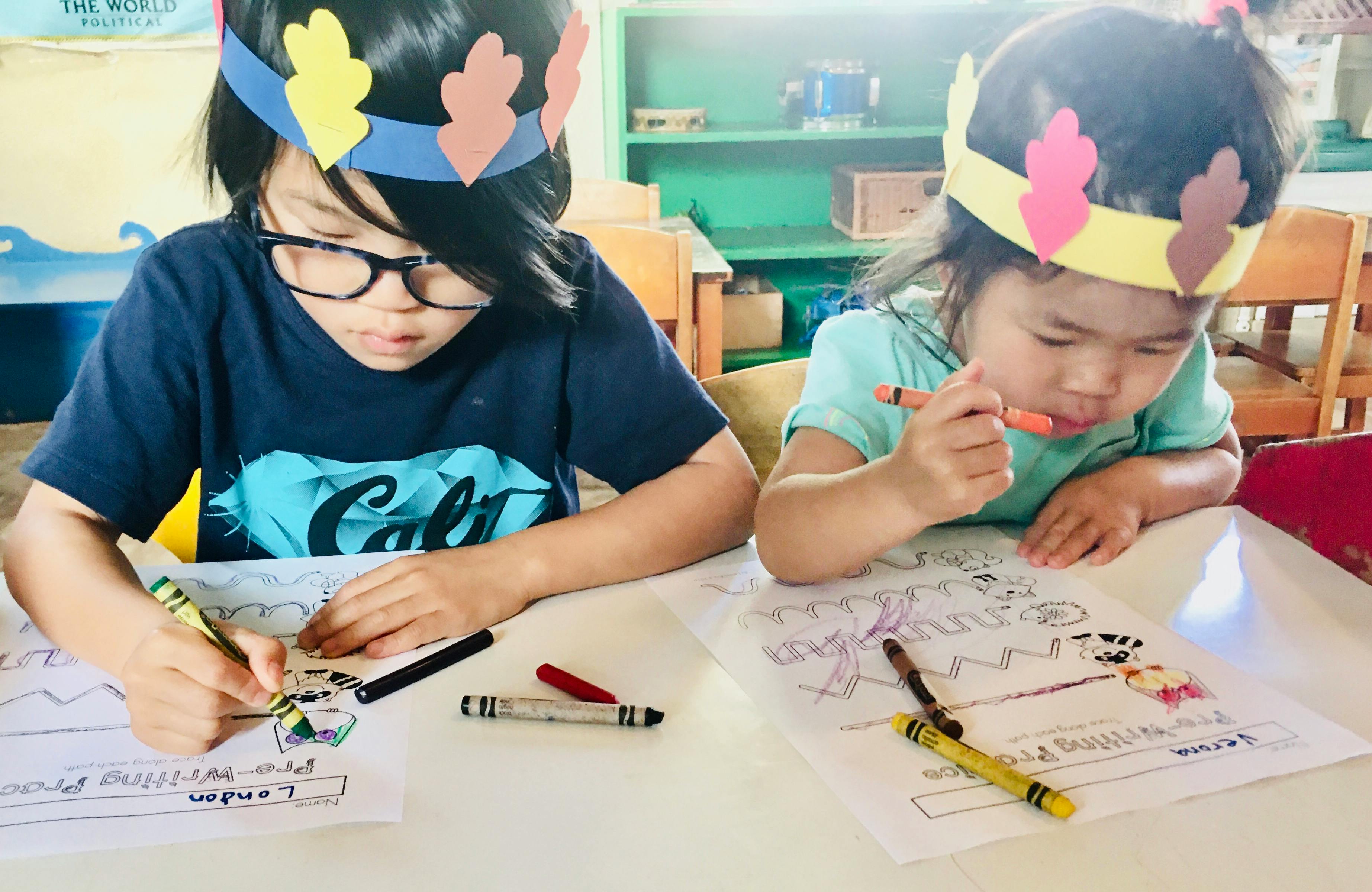 Two children wearing paper crowns coloring at a table