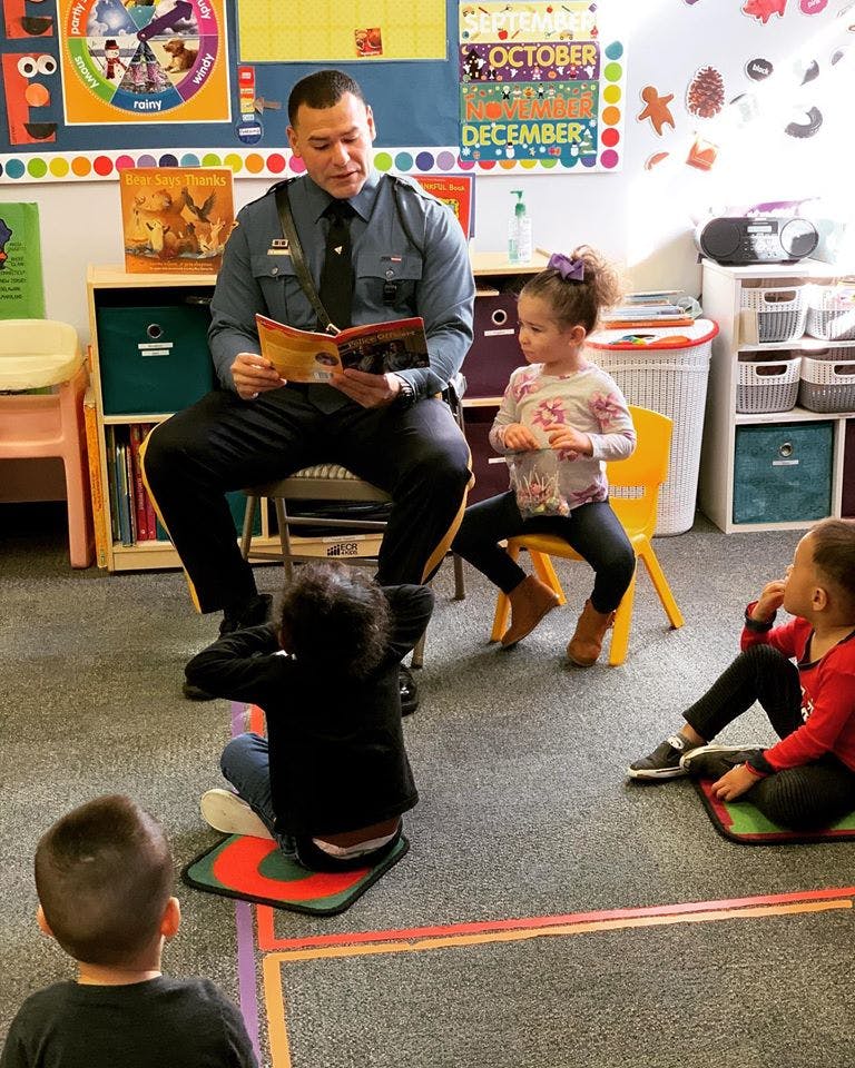 Person in uniform reading a book to children in a classroom
