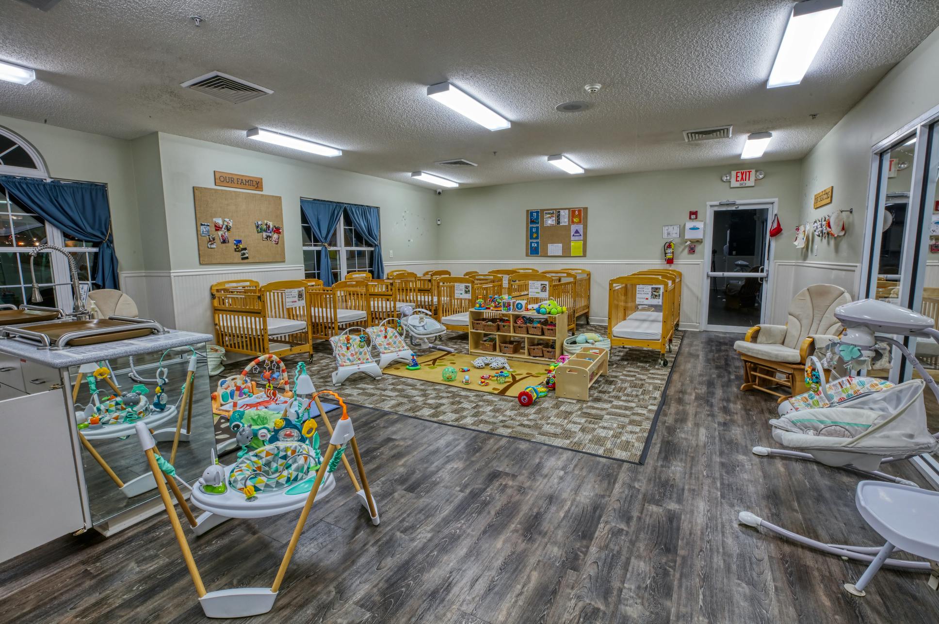 A room in a daycare center with multiple cribs, infant play equipment, and a changing station