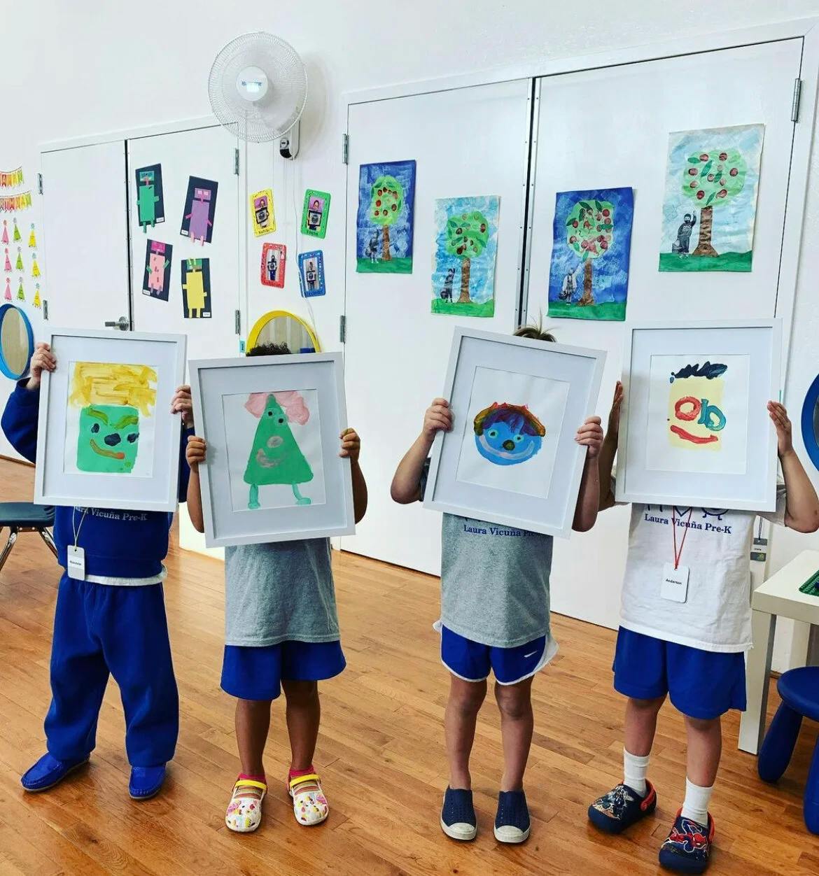 Four children holding up framed paintings in a classroom