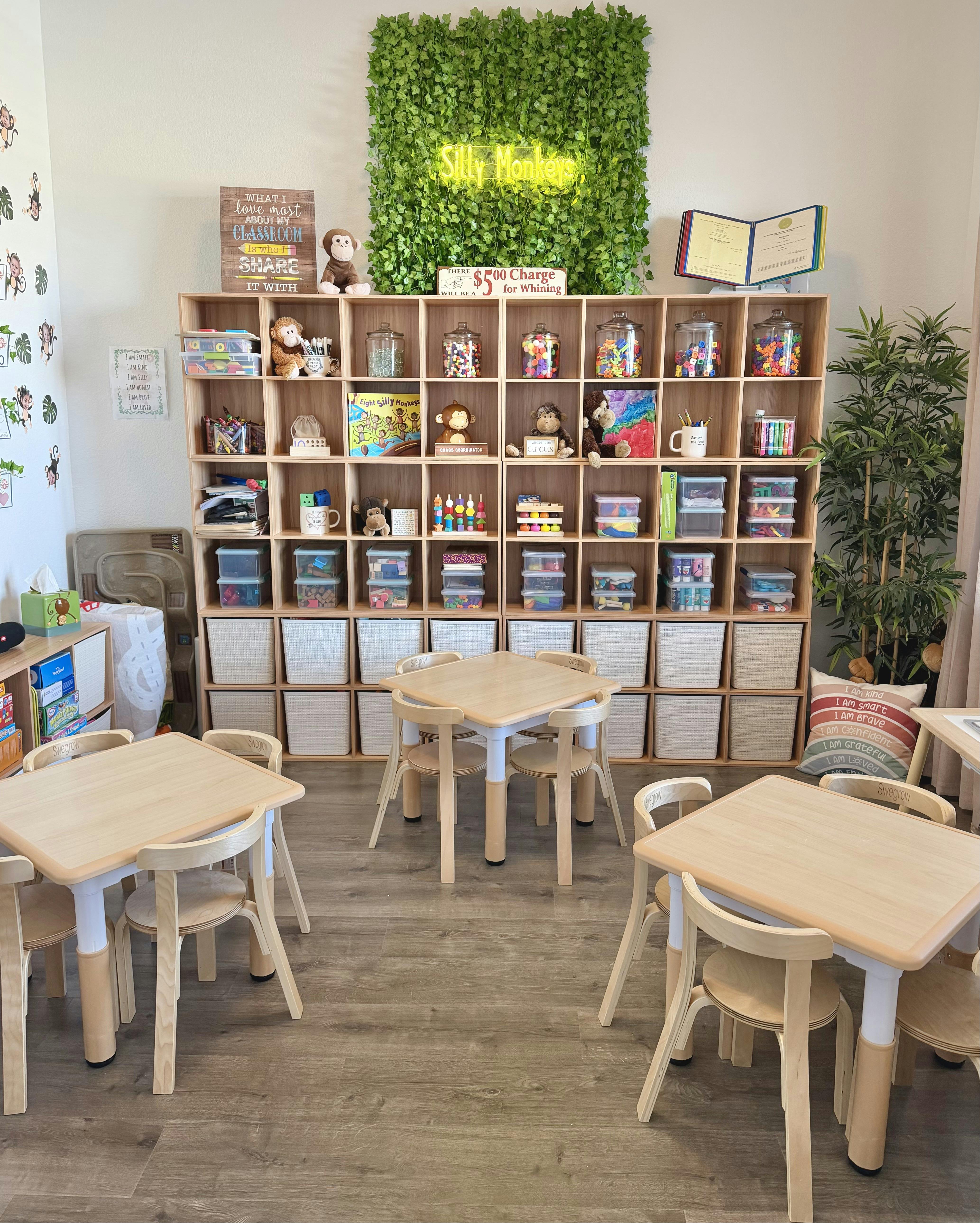 Children's classroom with small tables and chairs, a large storage shelf, and neon sign