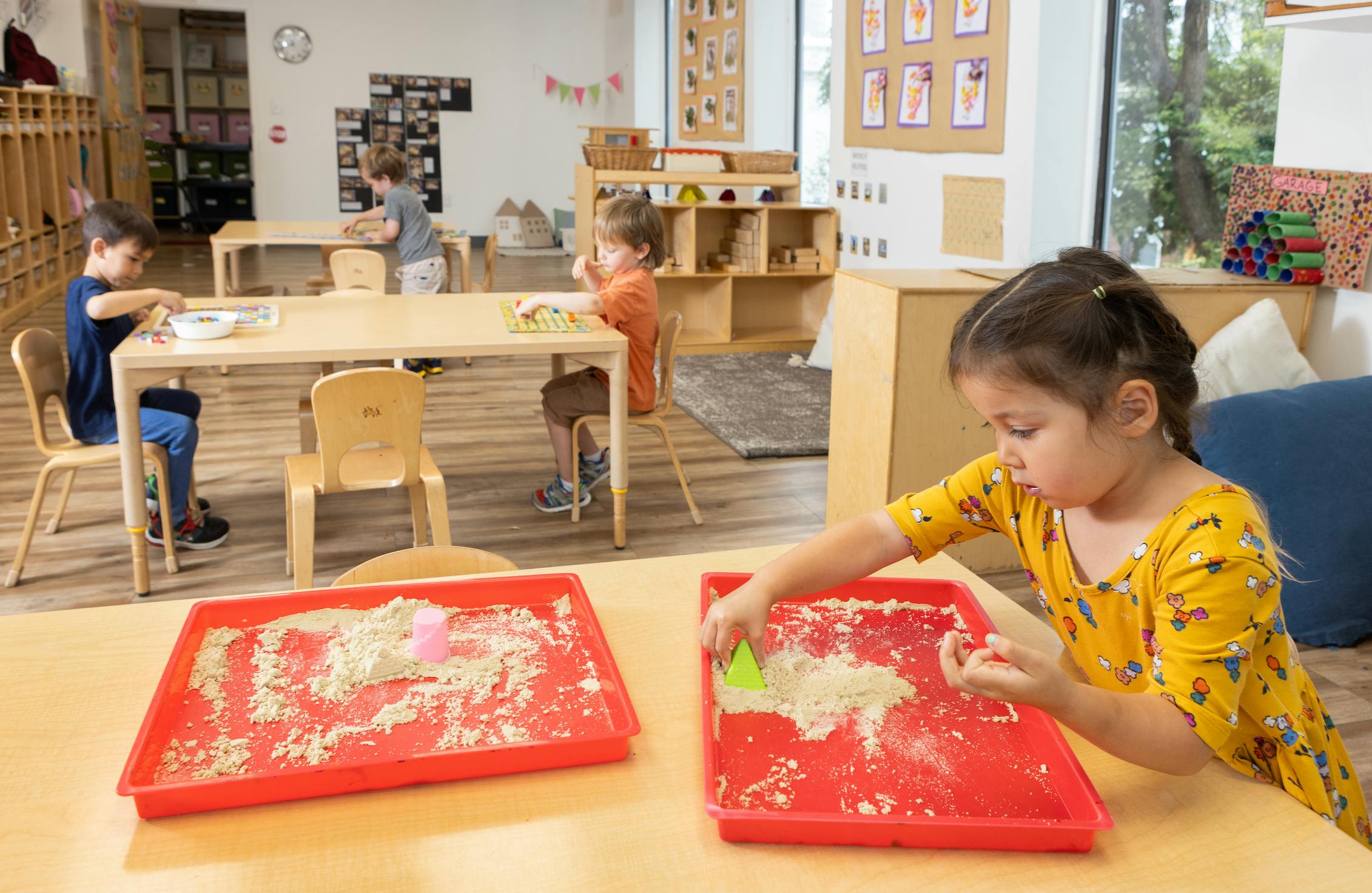 Child playing with sand in a red tray in a classroom