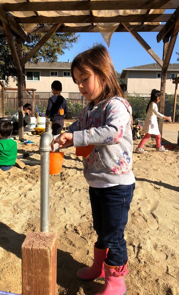 Child playing with a water pump in a sandbox