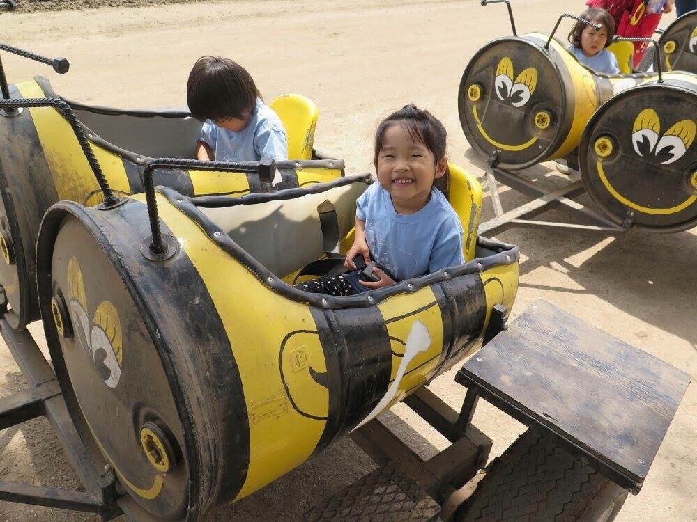 Child smiling in a bee-themed ride with another child in the background