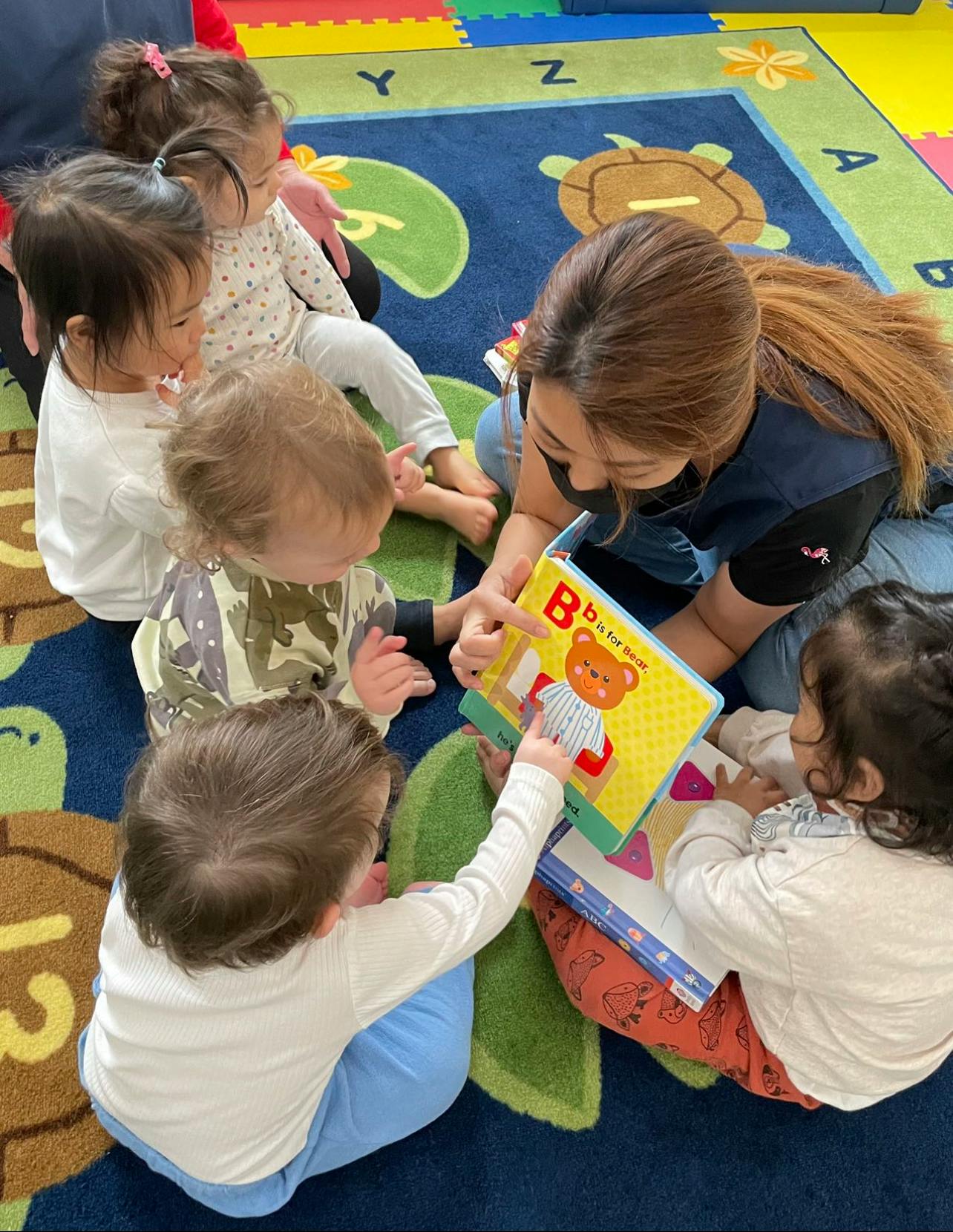 Adult reading a book to several children on a rug