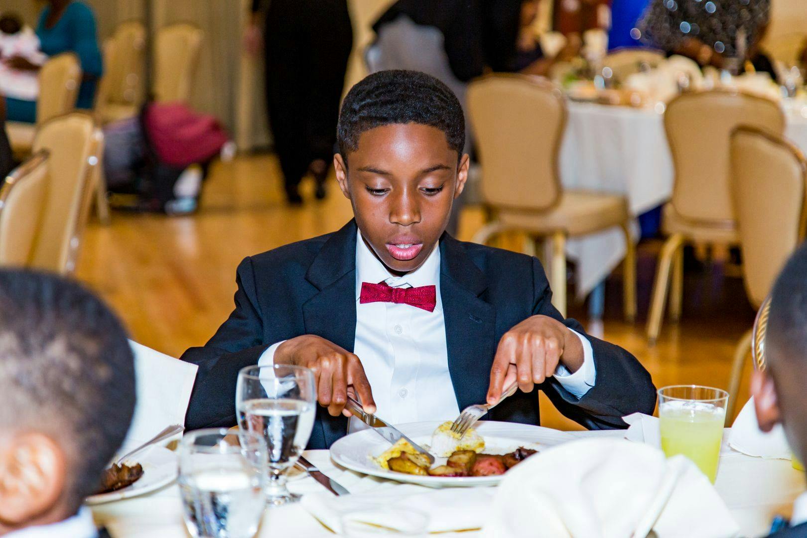 Child in a suit and bow tie eating a meal at a table