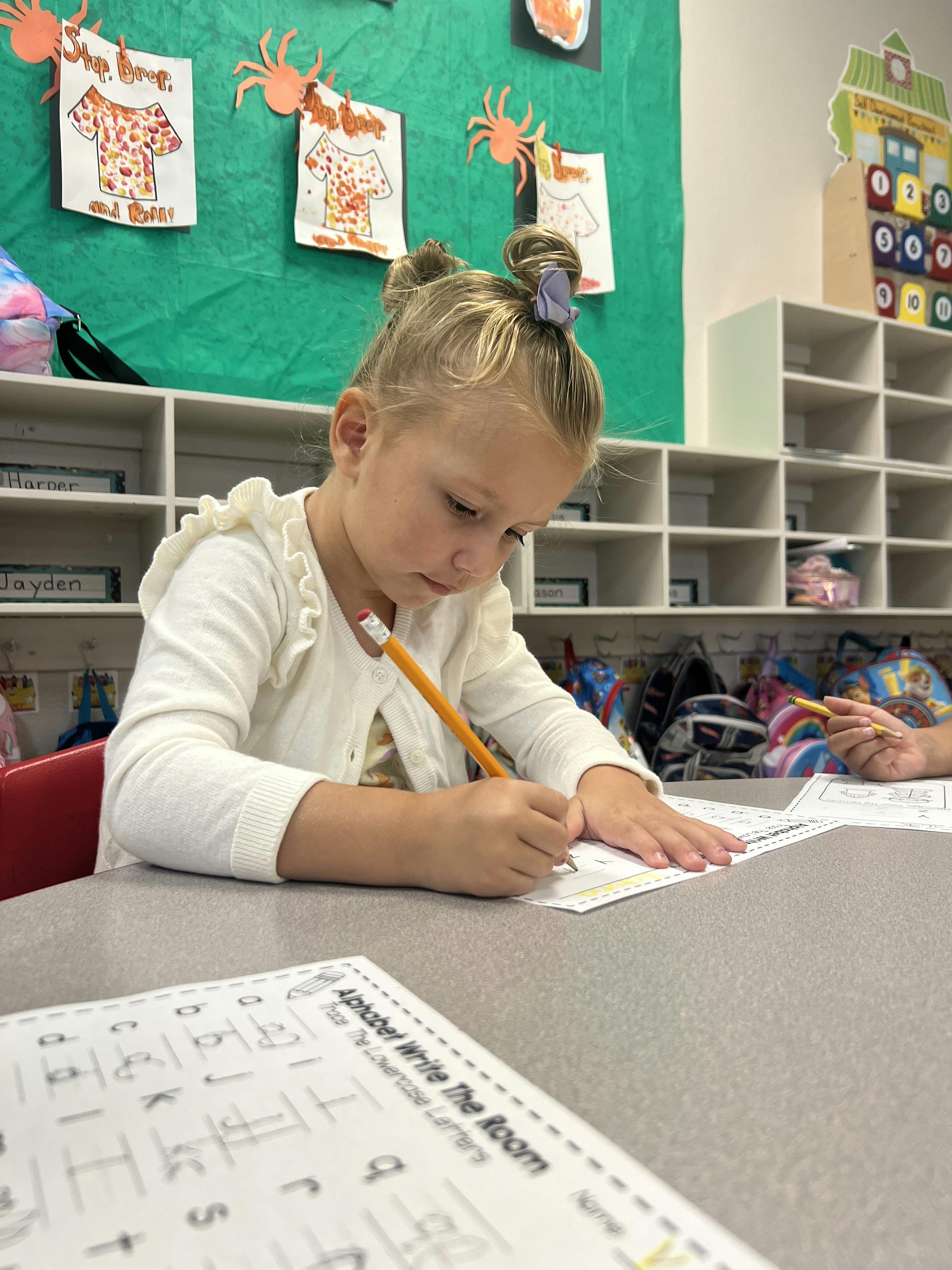Child writing with a pencil at a desk in a classroom