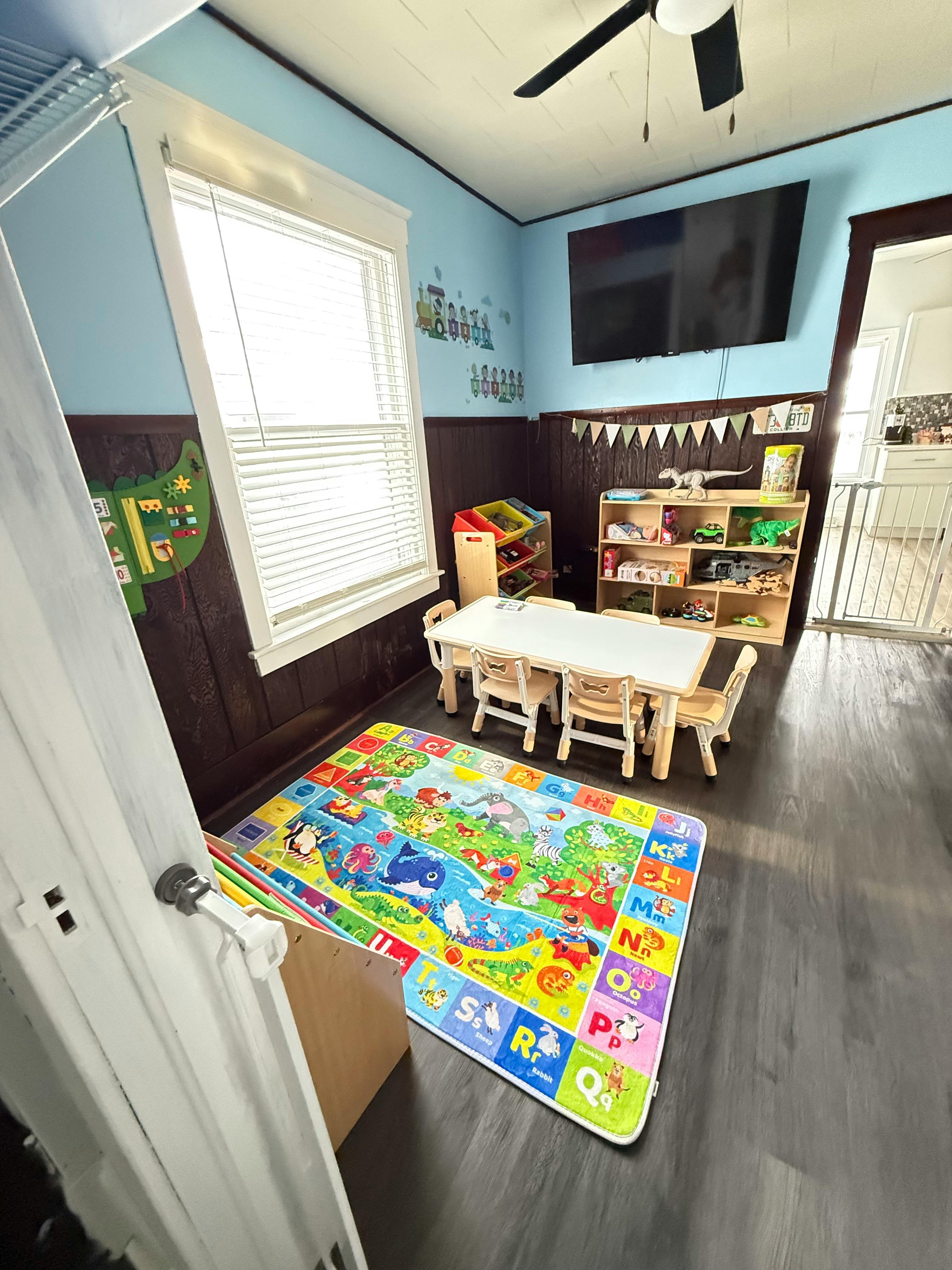 Playroom with a small table and chairs, toy shelves, and a colorful playmat