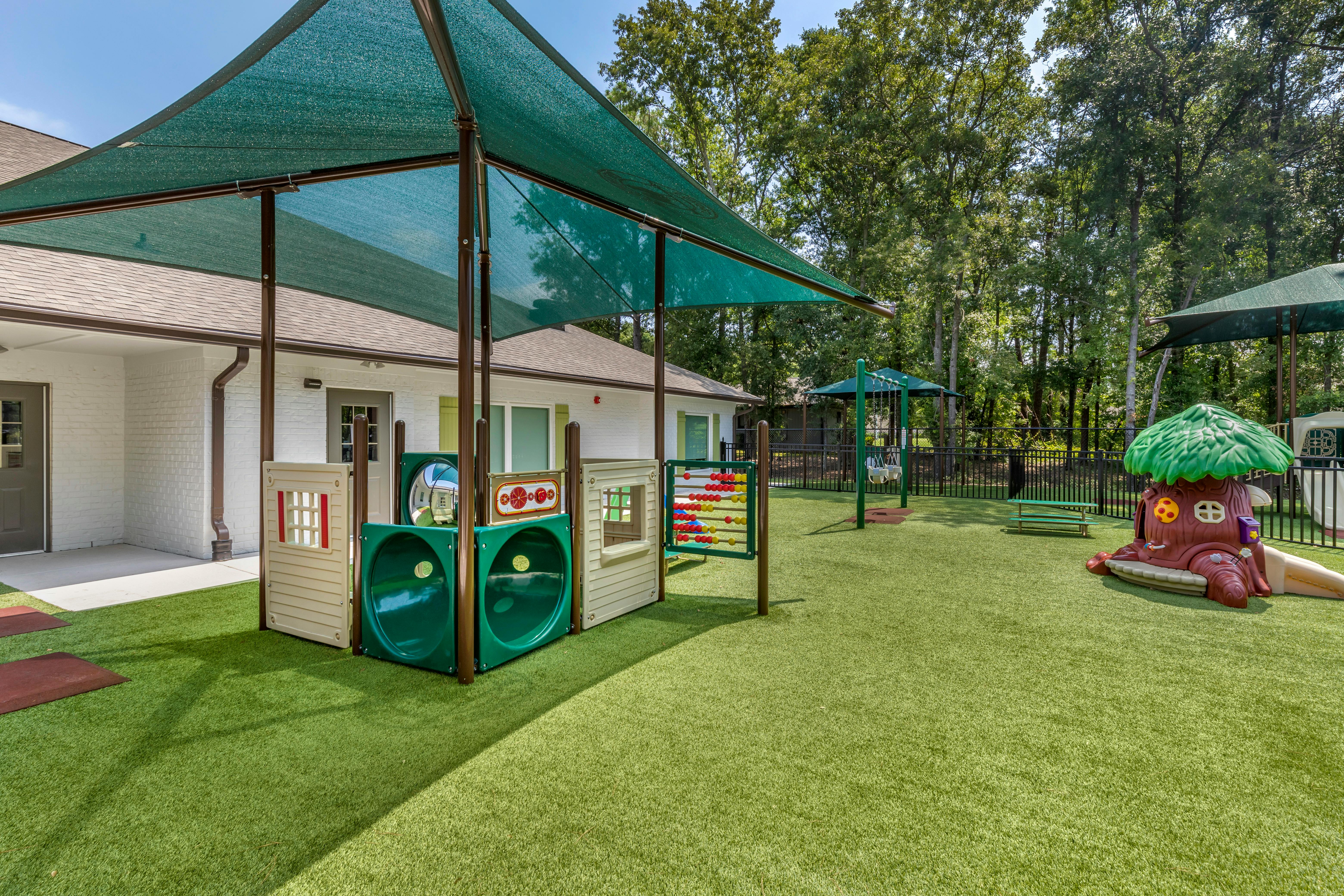 Outdoor playground with artificial turf, play structures, and a green canopy shade