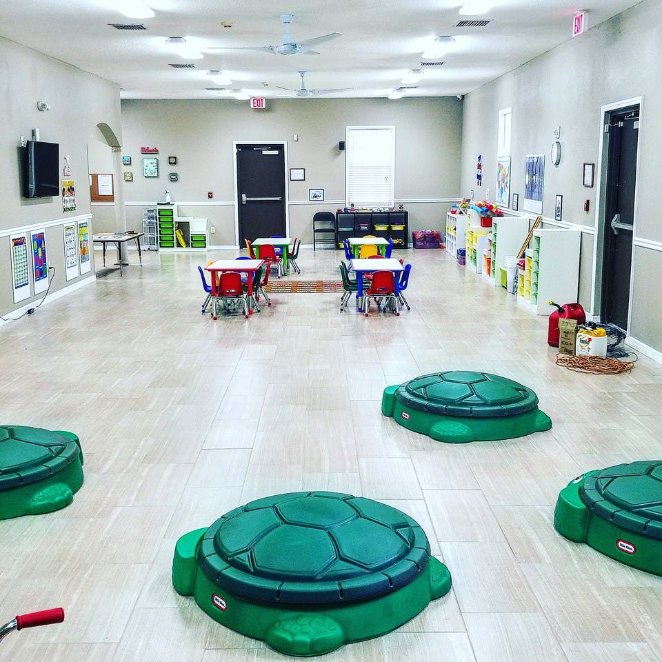Empty classroom with small tables and chairs, and turtle-shaped play items on the floor