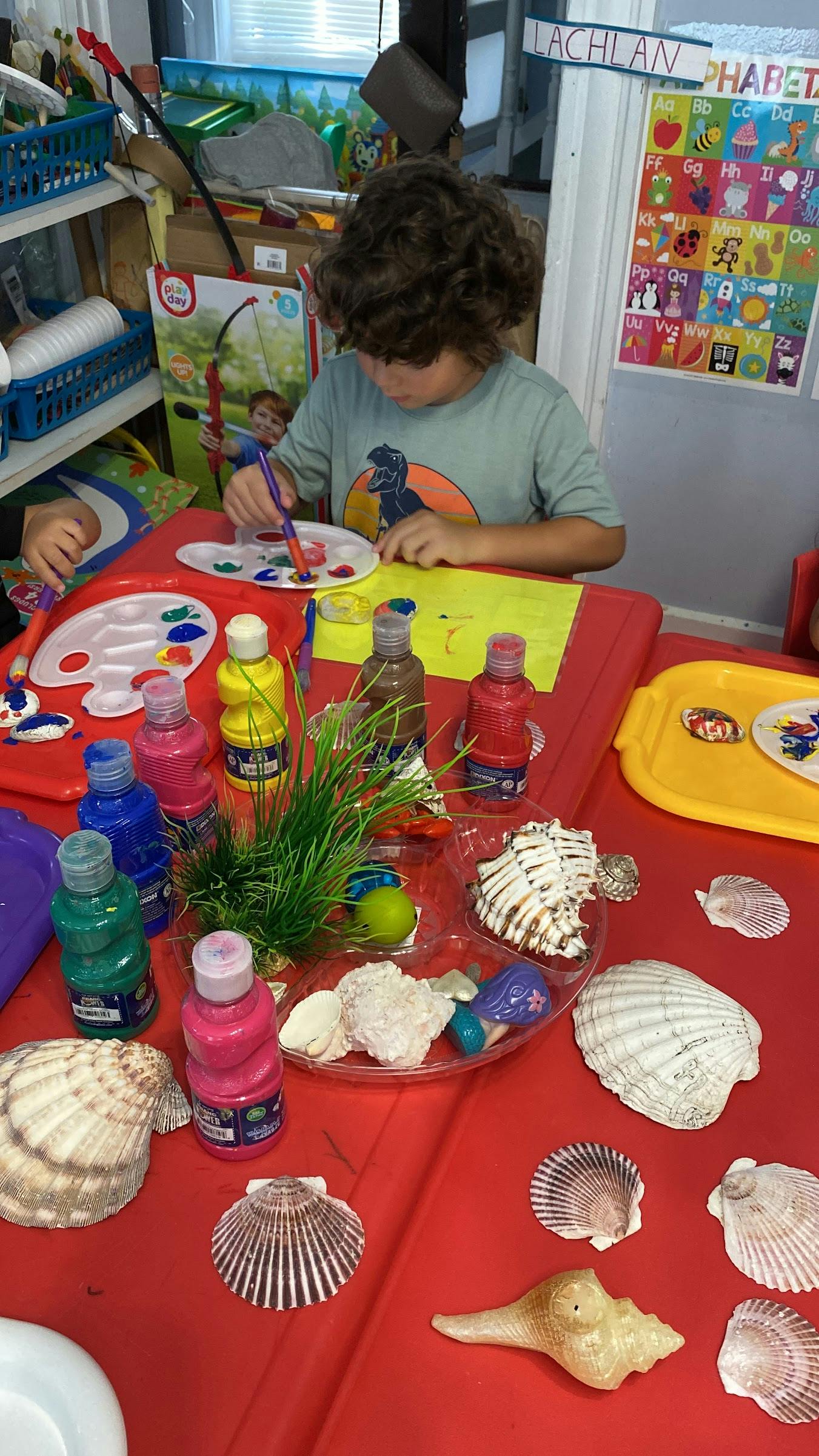 Child painting seashells at a table
