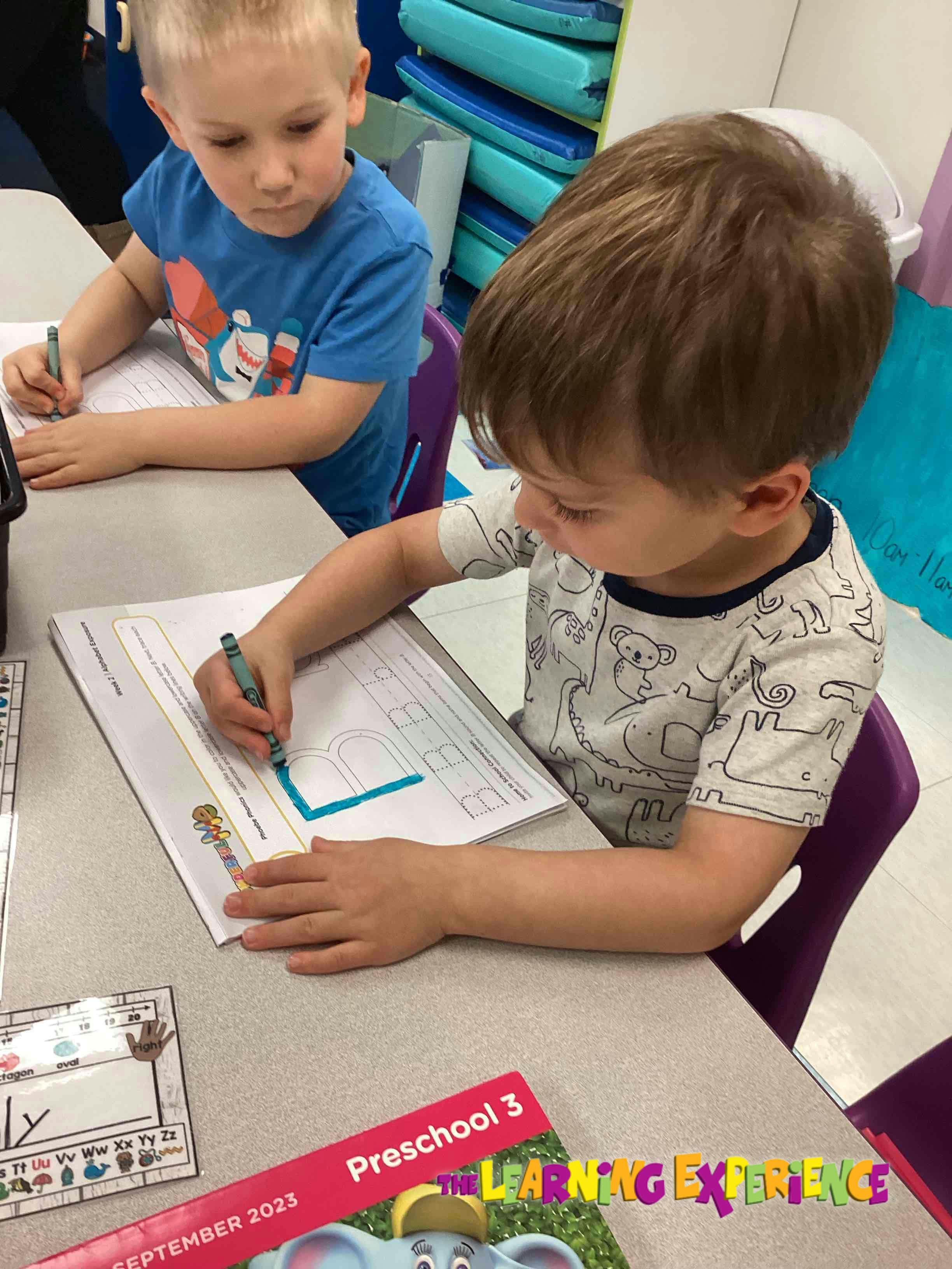 Two children writing at a table in a classroom