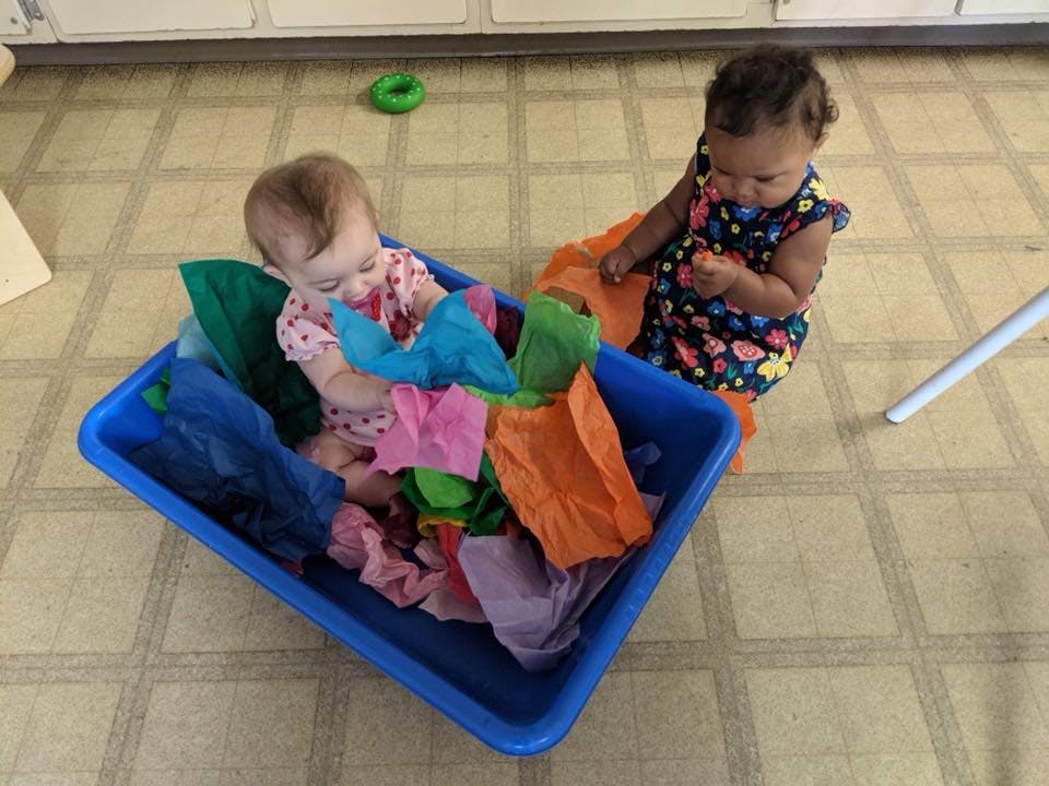 Two children playing with colorful fabric in a blue bin