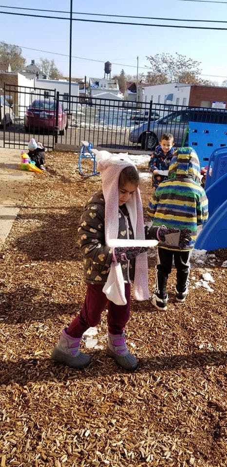 Child in a pink scarf holding a white object, with other children in the background