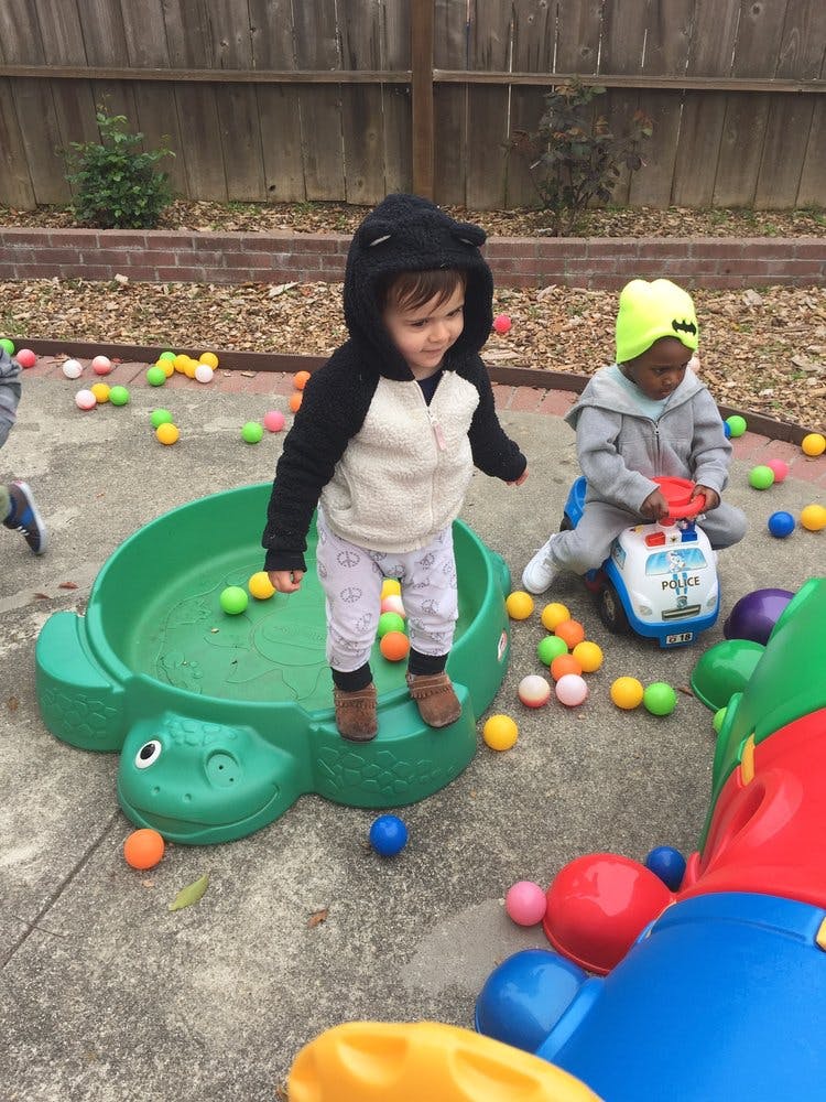 Child standing in a turtle-shaped sandbox, another child on a toy car