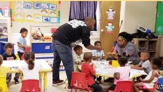 Adults interacting with children at tables in a classroom