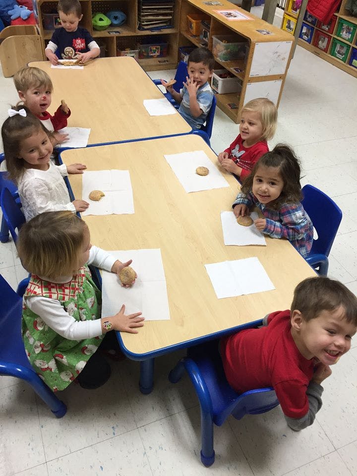 Children sitting at tables with cookies on paper in a classroom