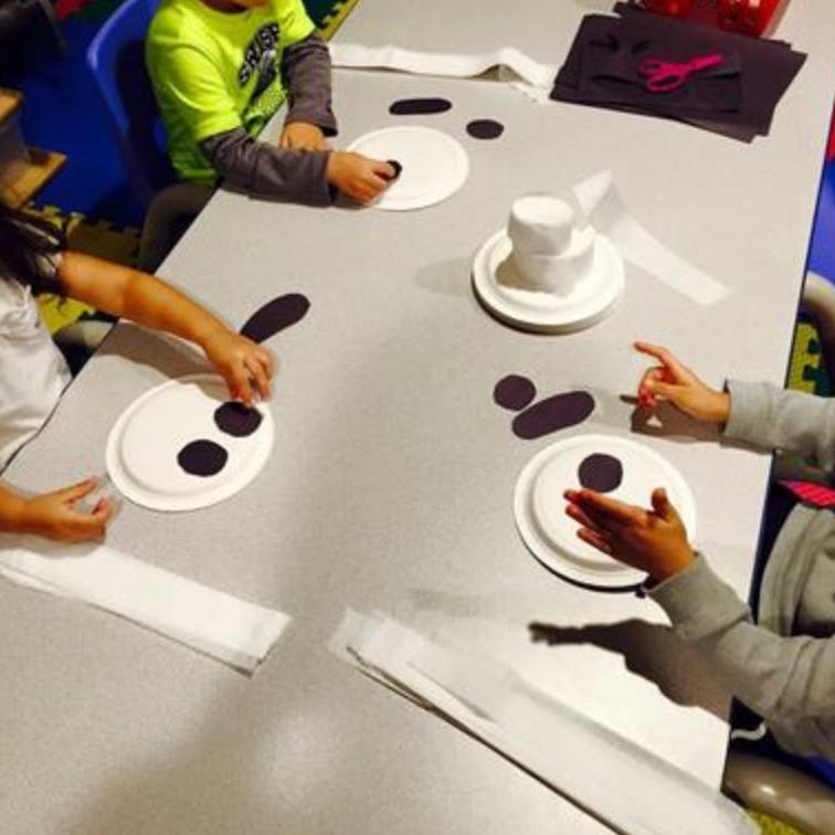Children making crafts with paper plates and cutouts at a table
