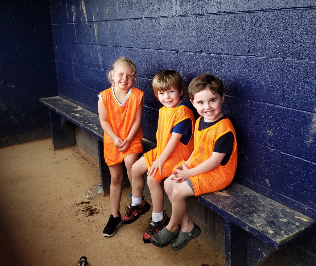 Three children in orange vests sitting on a bench